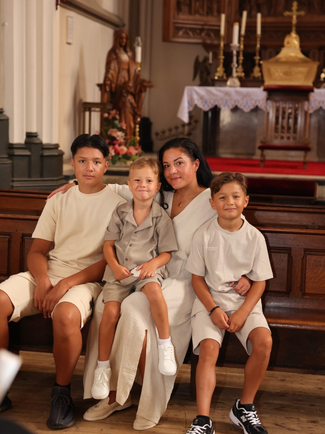 Een vrouw en drie kinderen zitten samen in een kerk, met beelden op de achtergrond.