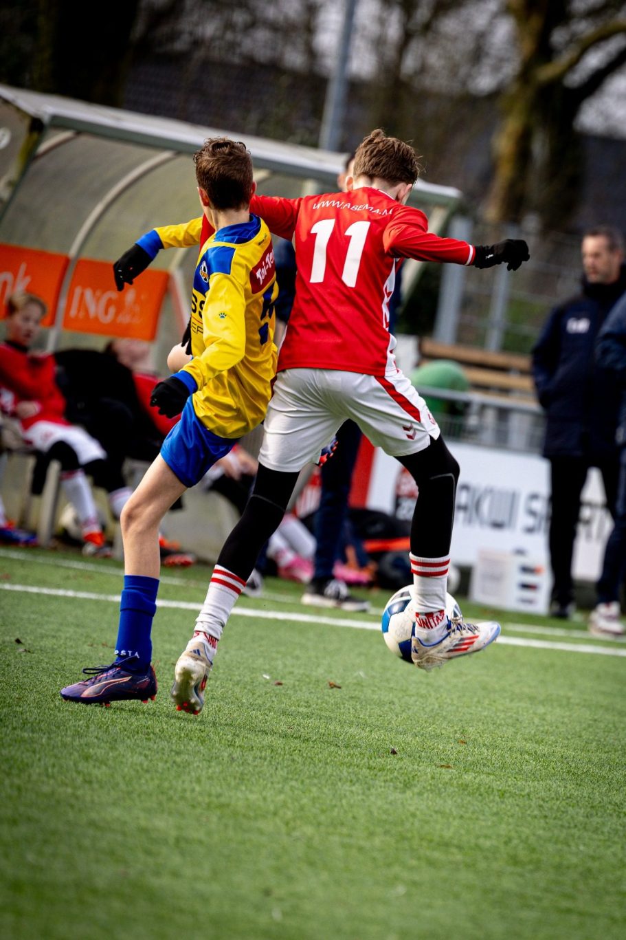Jongens in sportkleding strijden om de bal tijdens een voetbalwedstrijd.
