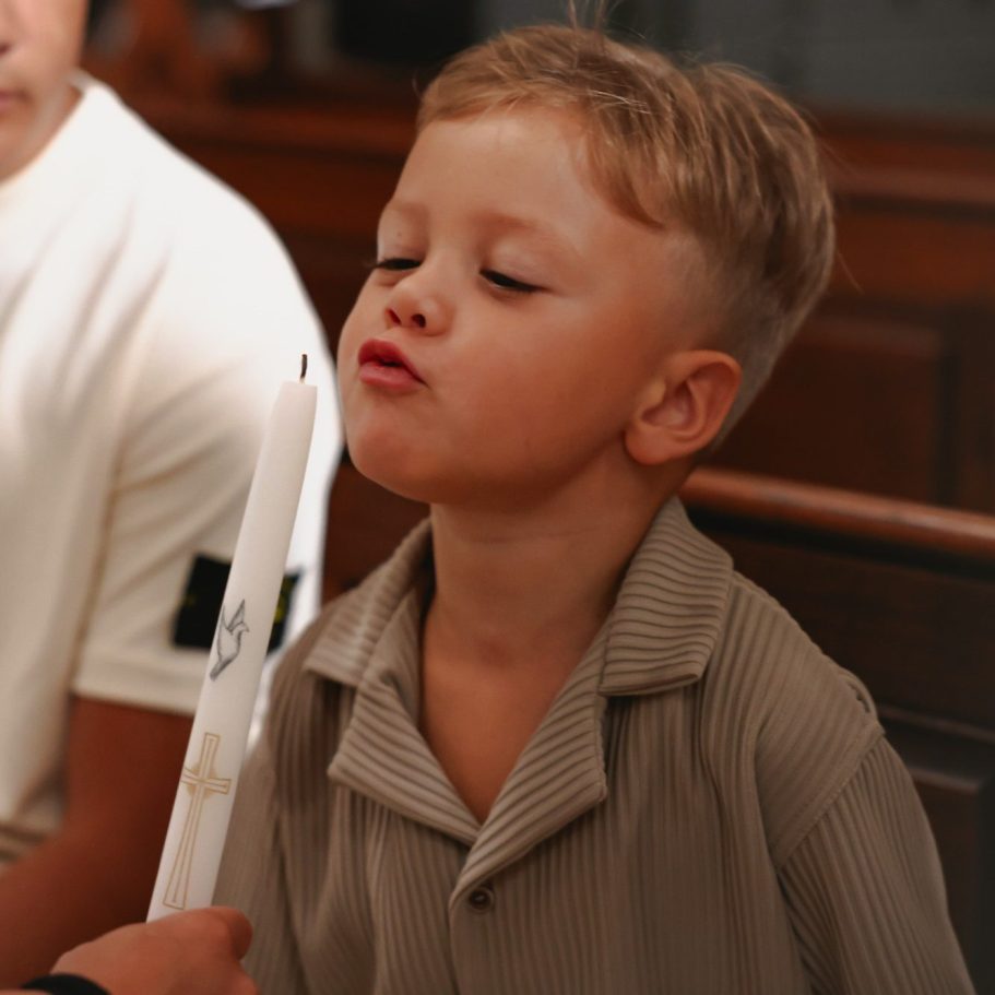 Jongentje blaast op een kaars terwijl hij in een kerk zit.