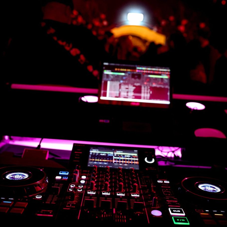 DJ-apparatuur met computer in een nachtclubsetting, sfeerverlichting op de achtergrond.