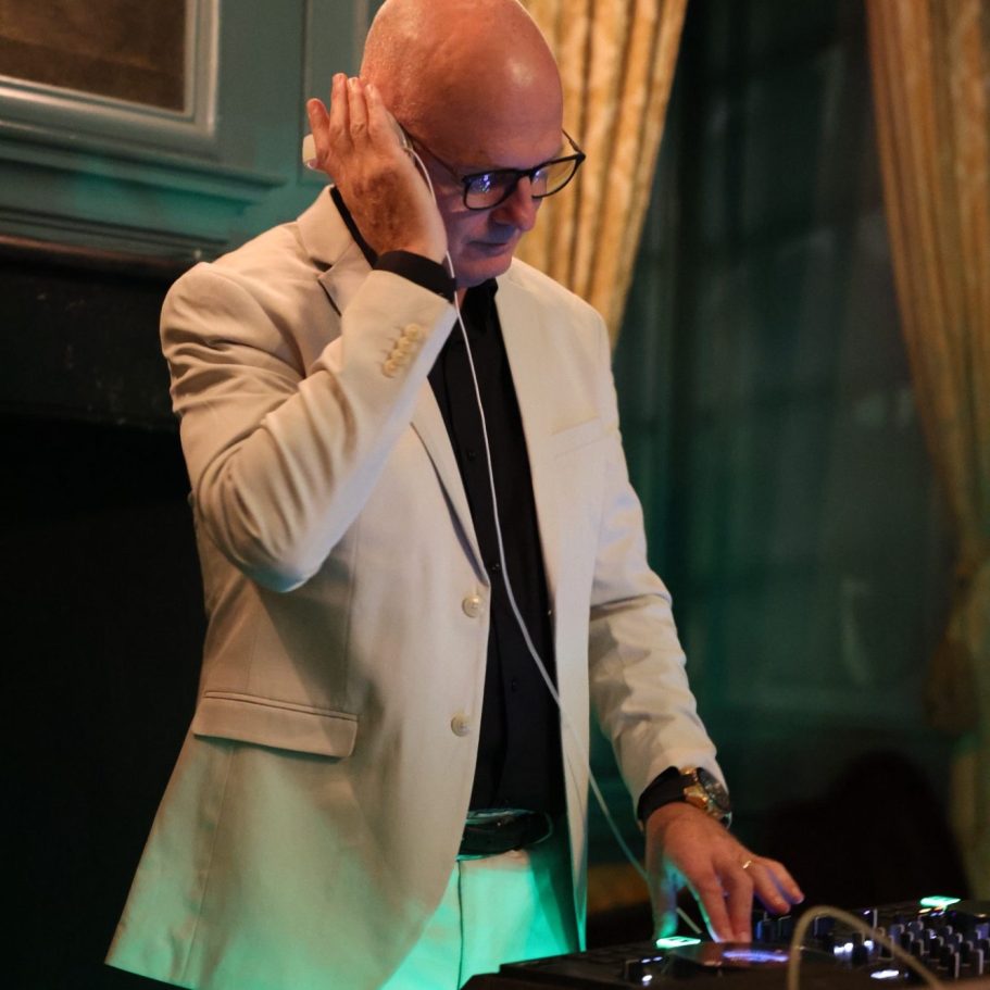 Een man in een wit pak draait muziek met een mixer in een sfeervolle ruimte.