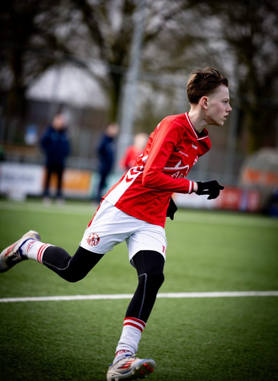 Jongen in een rood voetbalshirt rent over een grasveld.