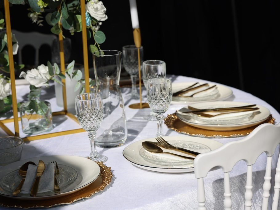 Elegante gedekte tafel met gouden bestek, witte borden en bloemenarrangementen.